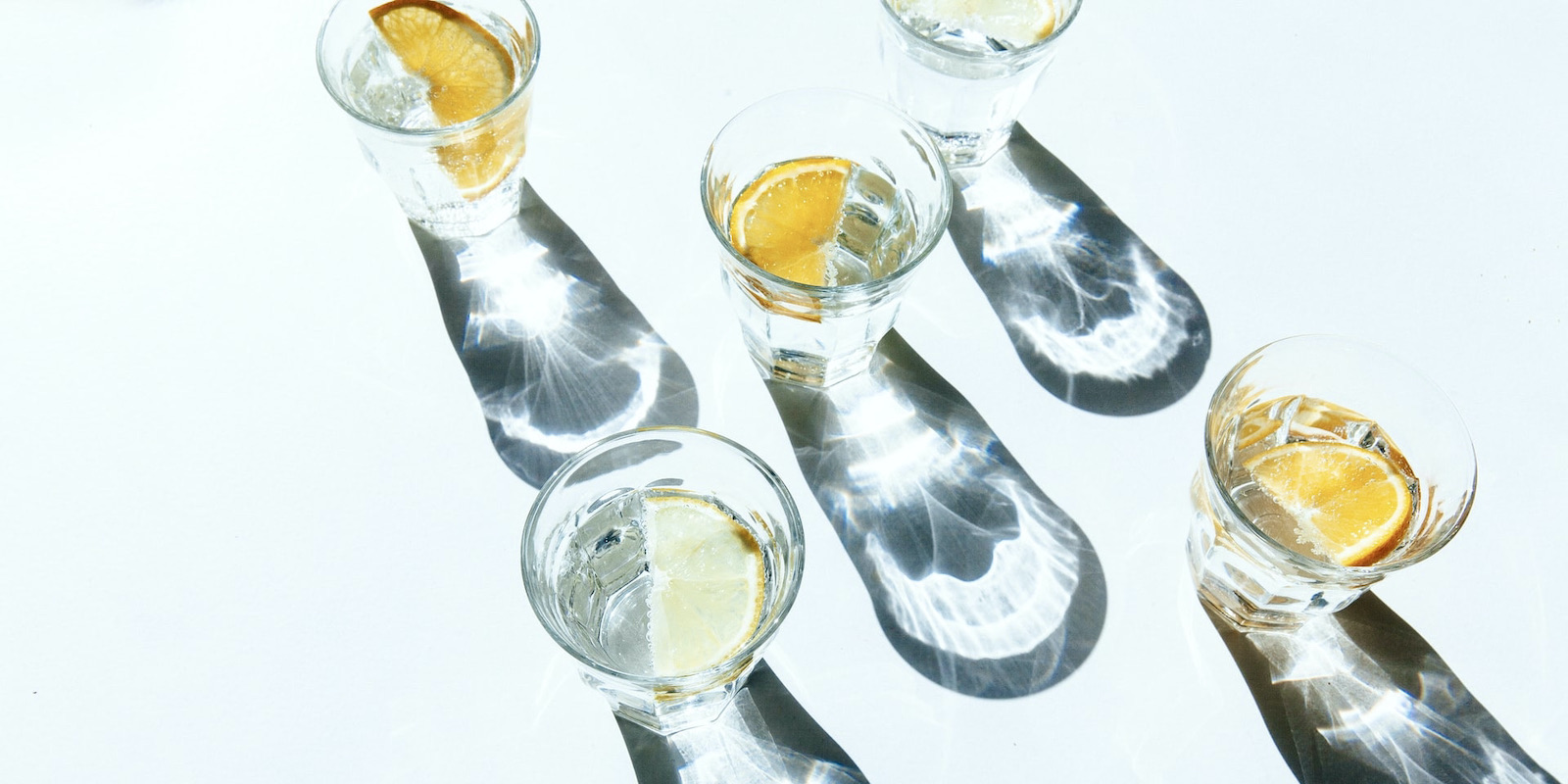 A bright photograph of water glasses with lemon slices in them creating shadows on an empty surface