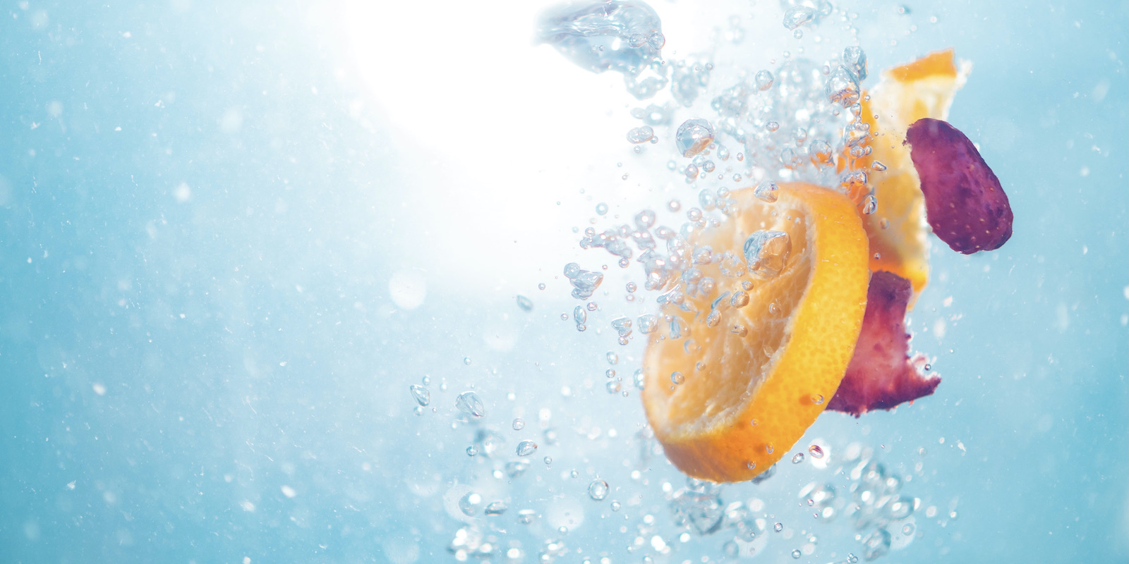 Submerged orange slices, lemon slices and strawberry slices float among air bubbles