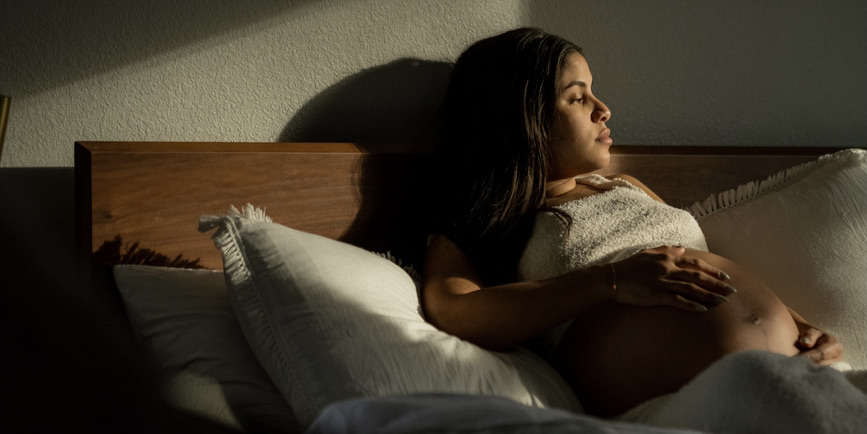 A young latin woman 40 weeks pregnant, resting and stretching in bed for the evening.
