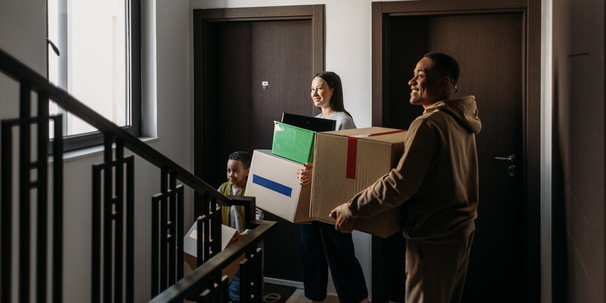 A family of three moving into new apartment together, carrying boxes with different stuff