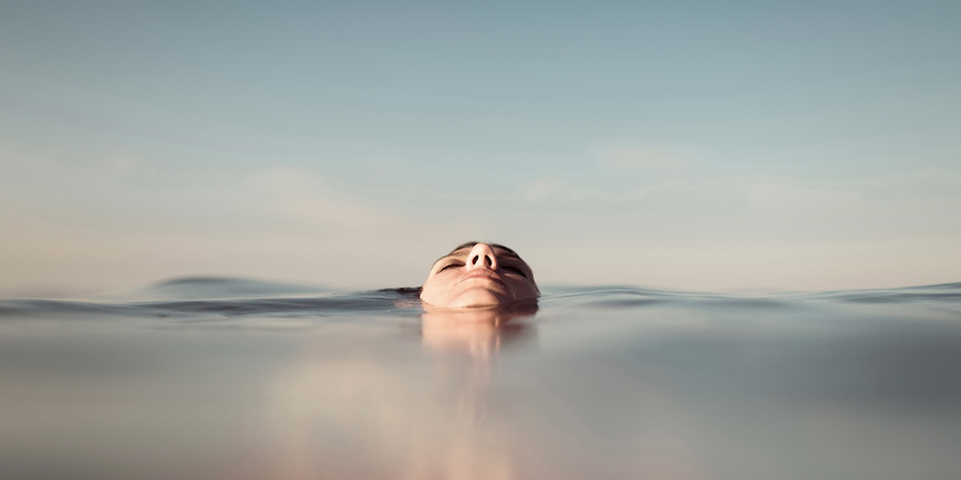 Color photograph of a minimal portrait of a woman's face floating in the sea during a sunny day of summer