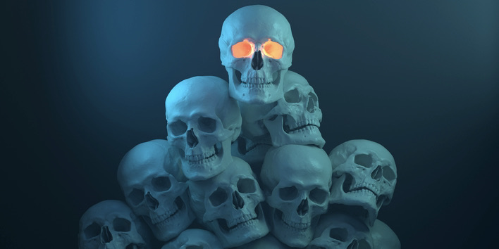 Pile of Glowing scary Halloween skulls in an eery blue background. The top skull has a glow from inside.