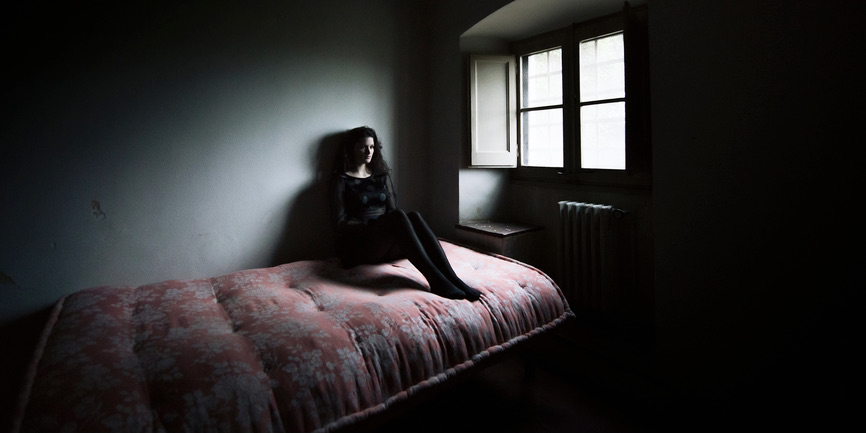 Wide angle portrait of sitting woman in a dark bedroom with soft window light