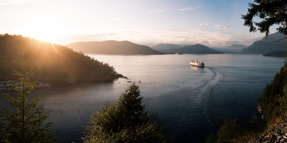 A cruise ship seen in the distance leaving a wide harbor in a mountain pass during sunset. 